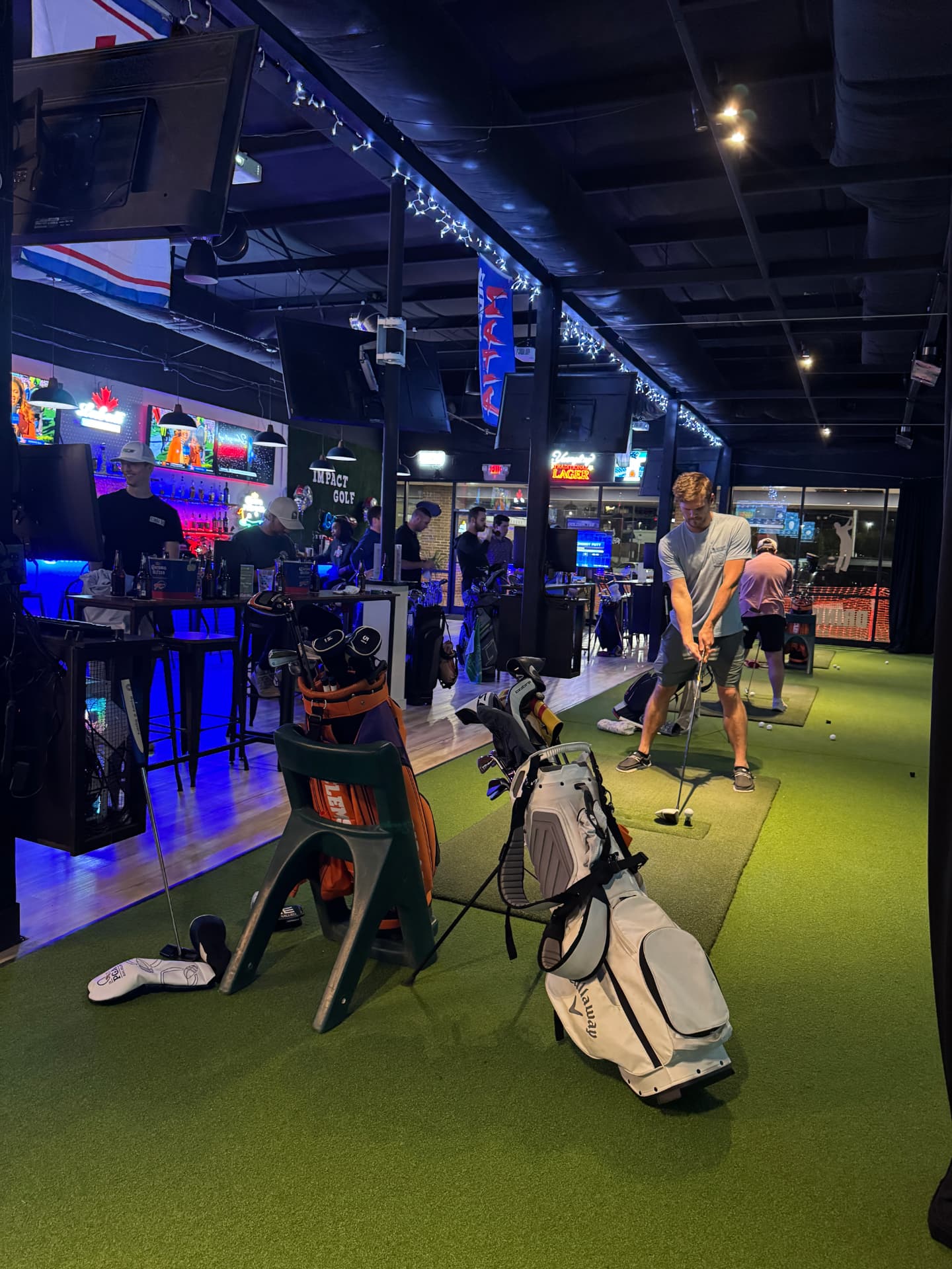 Interior of Impact Golf Lounge showing golfers at simulator bays and the bar area